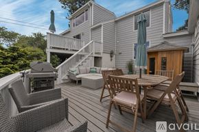 York house for rent - A wooden deck with a table and chairs is surrounded by a house and trees.