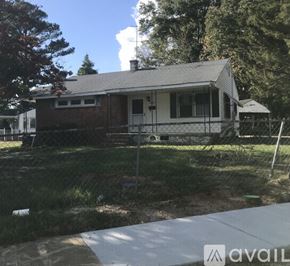 Kinston house for rent - A small house with a white door and a chimney is surrounded by a fence.