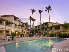 Phoenix condo for rent - A swimming pool is surrounded by chairs and palm trees in front of apartment buildings.