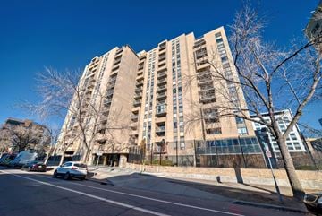 Calgary house for rent - A tall building with a lot of windows is surrounded by trees and cars on the street.