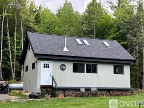 Middlesex house for rent - A small house with a white door and windows is surrounded by trees.