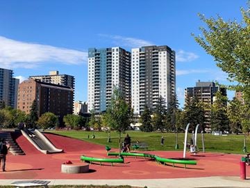 Saskatoon apartment for rent - A playground with a red surface and green benches is surrounded by tall buildings.