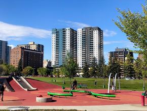 Saskatoon apartment for rent - A playground with a red surface and green benches is surrounded by tall buildings.