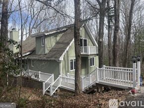 Dillard house for rent - A house with a green roof and white railings is surrounded by trees.