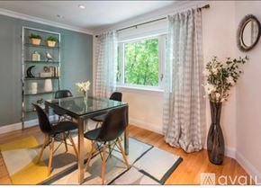 Brookline apartment for rent - A glass dining table with four chairs and a vase of flowers on a rug in front of a window.