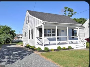 Pocomoke house for rent - A small white house with a grey roof and a porch.
