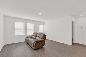 San Antonio house for rent - A brown leather sofa sits in a spacious room with wooden floors and white walls.