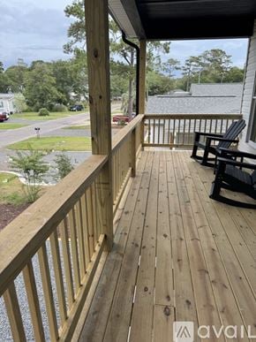 Oak Island house for rent - A wooden deck with a bench and a view of a street and trees.