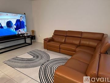 Miami house for rent - A living room with a brown leather couch and a television playing a movie.