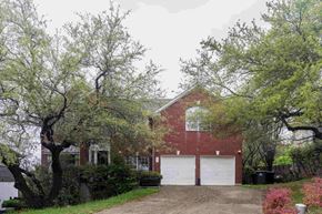 Austin house for rent - A red brick house with a white garage door is surrounded by trees.