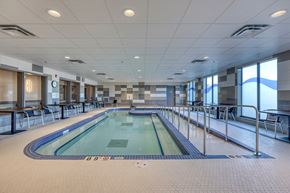 Leduc apartment for rent - A large indoor swimming pool with a blue tiled edge and a white tiled floor.