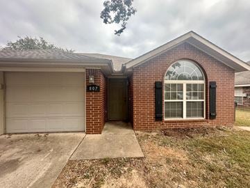 Rogers house for rent - A brick house with a white garage door and a window with black shutters.