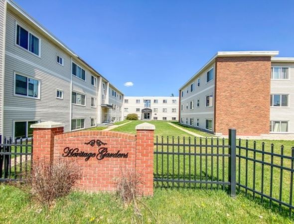Edmonton apartment for rent - A brick sign that says "Whispering Gardens" is in front of a black fence.