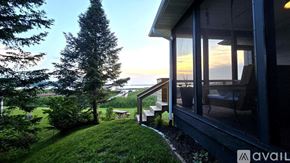 Onekama house for rent - A house with a balcony overlooks a green lawn and trees.