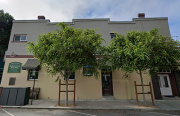 Half Moon Bay apartment for rent - A building with a green sign on the left side and a tree in front of it.