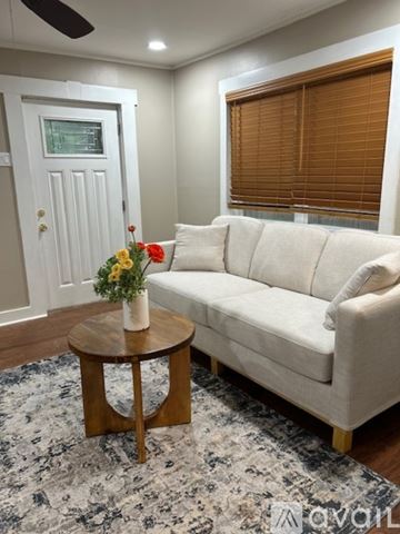 Little Rock house for rent - A living room with a white couch, a round wooden table with a vase of flowers on it, and a rug on the floor.