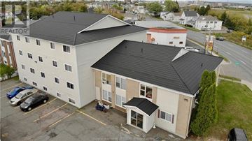 Moncton apartment for rent - A large white building with a black roof and a parking lot in front.