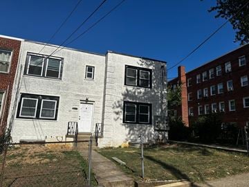 Washington apartment for rent - A white two-story building with a grey roof and a white door is surrounded by a grassy area and a sidewalk.