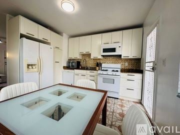 Miami Beach apartment for rent - A kitchen with white cabinets and a glass table.
