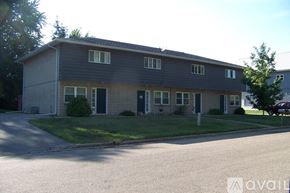 Pekin townhouse for rent - A two-story building with a grey roof and a parking lot in front.