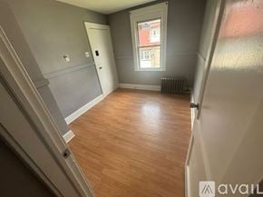 Hillside apartment for rent - A room with wooden flooring and a window with a view of a building outside.