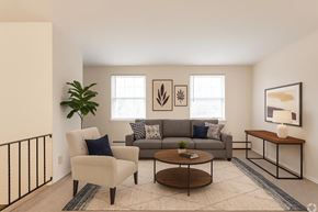 Cedar Grove apartment for rent - A living room with a grey couch, a white chair, a wooden coffee table, and a black railing.