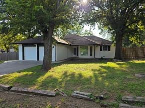 Harrah house for rent - A house with a white garage door is surrounded by trees.