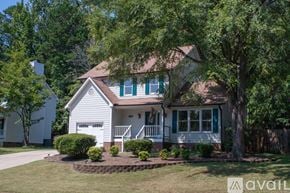 Durham house for rent - A house with a white exterior and green shutters is surrounded by trees and has a small front yard with a flower bed.
