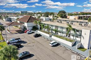 Kissimmee apartment for rent - A parking lot with cars and a white building with palm trees in front.