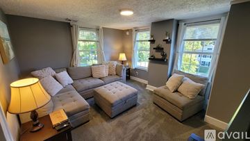 Branford apartment for rent - A living room with a grey couch, a white ottoman, and a lamp on a side table.