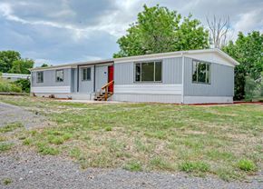 Colorado City house for rent - A grey house with a red door is surrounded by grass and trees.