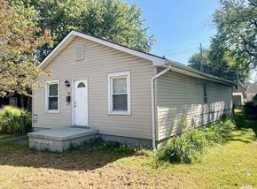New Albany house for rent - A small house with a white door and windows is surrounded by greenery.
