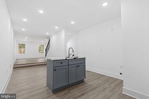 Baltimore house for rent - A kitchen island with a sink is in the middle of a room with white walls and wood flooring.