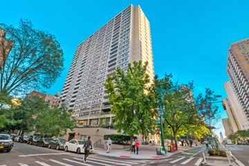 New York apartment for rent - A tall building is surrounded by trees and cars on the street.