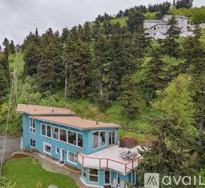 Anchorage apartment for rent - A blue house with a balcony is surrounded by green trees.