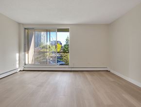 Calgary apartment for rent - A room with a sliding glass door leading to a balcony with a view of a blue car and trees.
