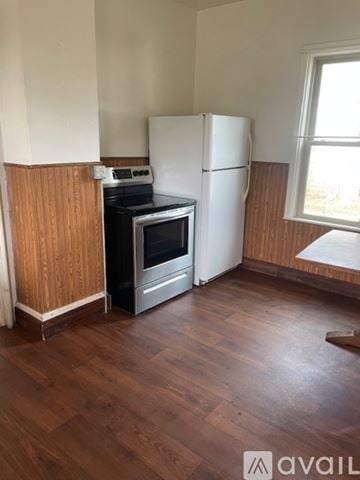 Watertown apartment for rent - A kitchen with a white fridge, black stove and oven, and wooden floors.