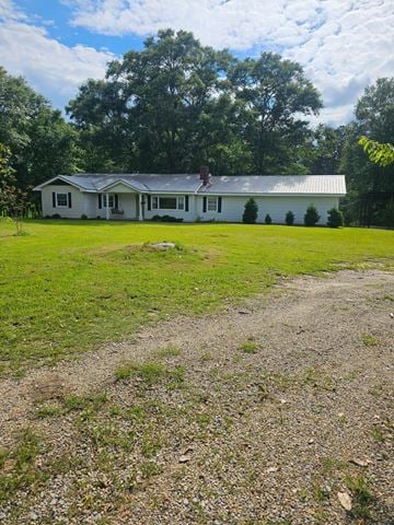 Poplarville house for rent - A white house with a grey roof is surrounded by a grassy area and trees.