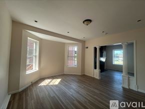 St. Louis house for rent - A spacious room with wooden floors and white walls, featuring a large window and a doorway leading to another room.