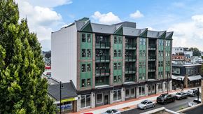 Chilliwack apartment for rent - A modern building with green trim is situated on a street corner.