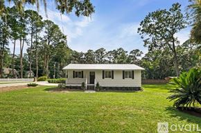 Savannah house for rent - A small white house with a porch is surrounded by greenery and trees.