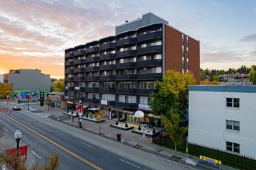 Calgary apartment for rent - A large building with a balcony on the second floor is in the middle of a street.