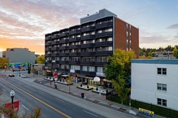 Calgary apartment for rent - A large building with a balcony on the second floor is in the middle of a street.