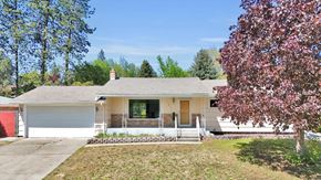 Spokane Valley house for rent - A house with a red garage door is surrounded by trees and has a small front yard.