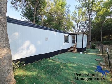 Laurel house for rent - A white mobile home with a black stripe at the bottom is surrounded by trees.