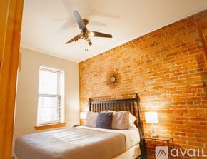 Boston apartment for rent - A bedroom with a brick wall and a bed with a white comforter.