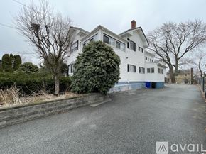 Malden apartment for rent - A white house with a blue door is surrounded by a grey wall and trees.