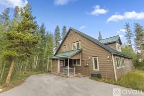 Breckenridge house for rent - A house with a green roof is surrounded by trees and has a driveway in front.