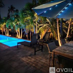 Oakland Park house for rent - A pool surrounded by palm trees and a house with a blue umbrella.