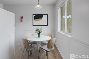 Muncie apartment for rent - A dining room with a white table and chairs, a framed picture on the wall, and a vase of flowers on the table.